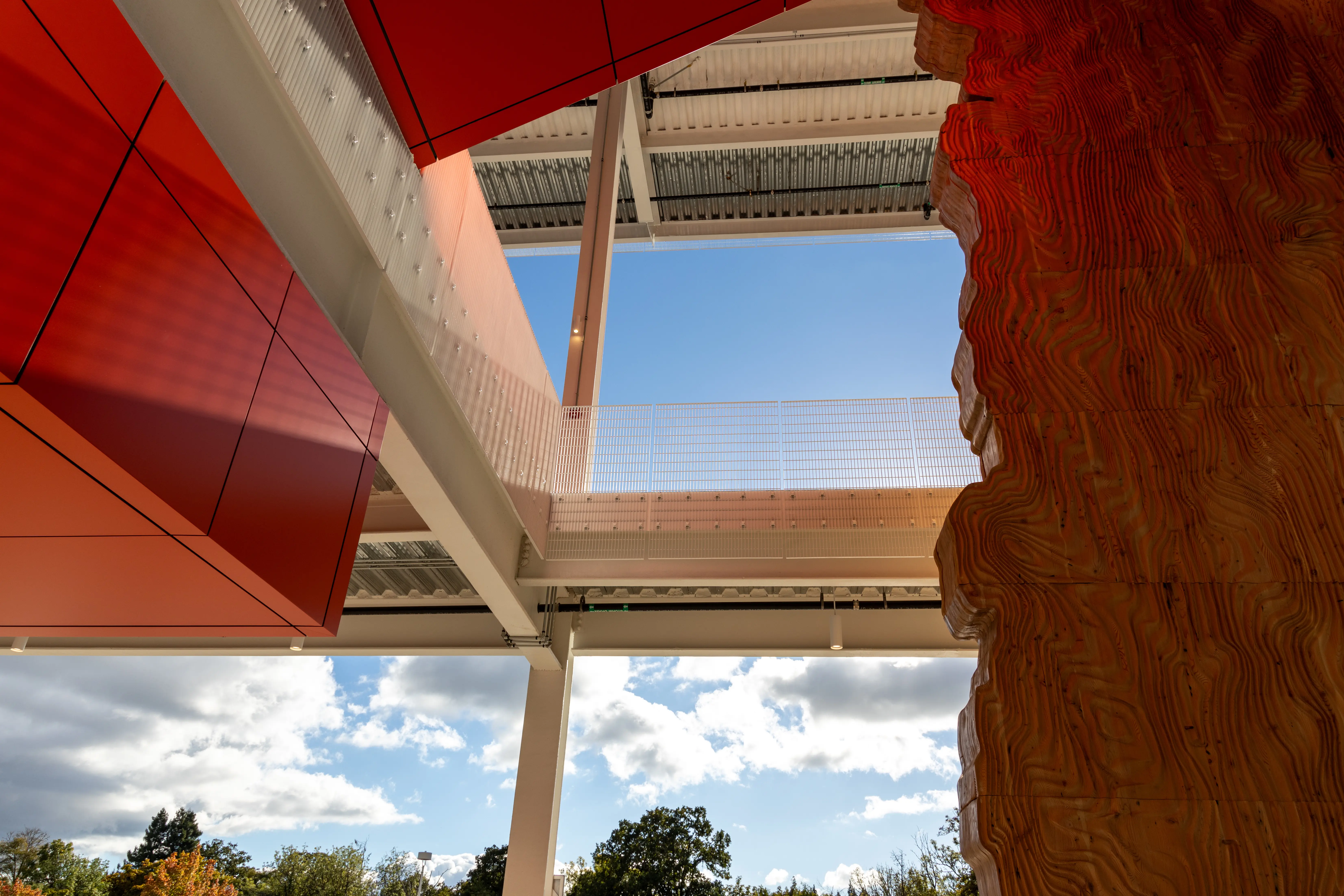 Look out from a building toward blue sky and white clouds. Massive piece of wood that is art installationon right side of image.
