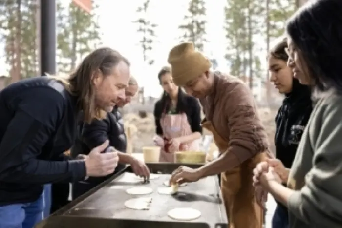 A group of people gathered around an outdoor griddle cooking tortillas