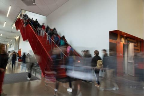 Busy indoor stairwell in LINC with people ascending and descending, creating motion blur that conveys movement and activity. 