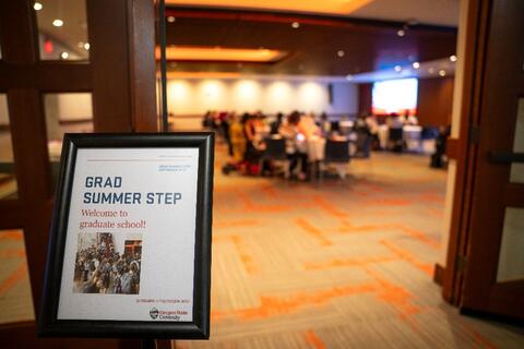 A "Grad Summer Step" welcome sign outside of a room with people sitting around